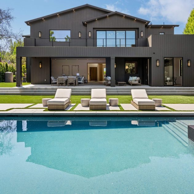 Luxury modern house with a swimming pool, sun loungers, and a spacious backyard on a sunny day.